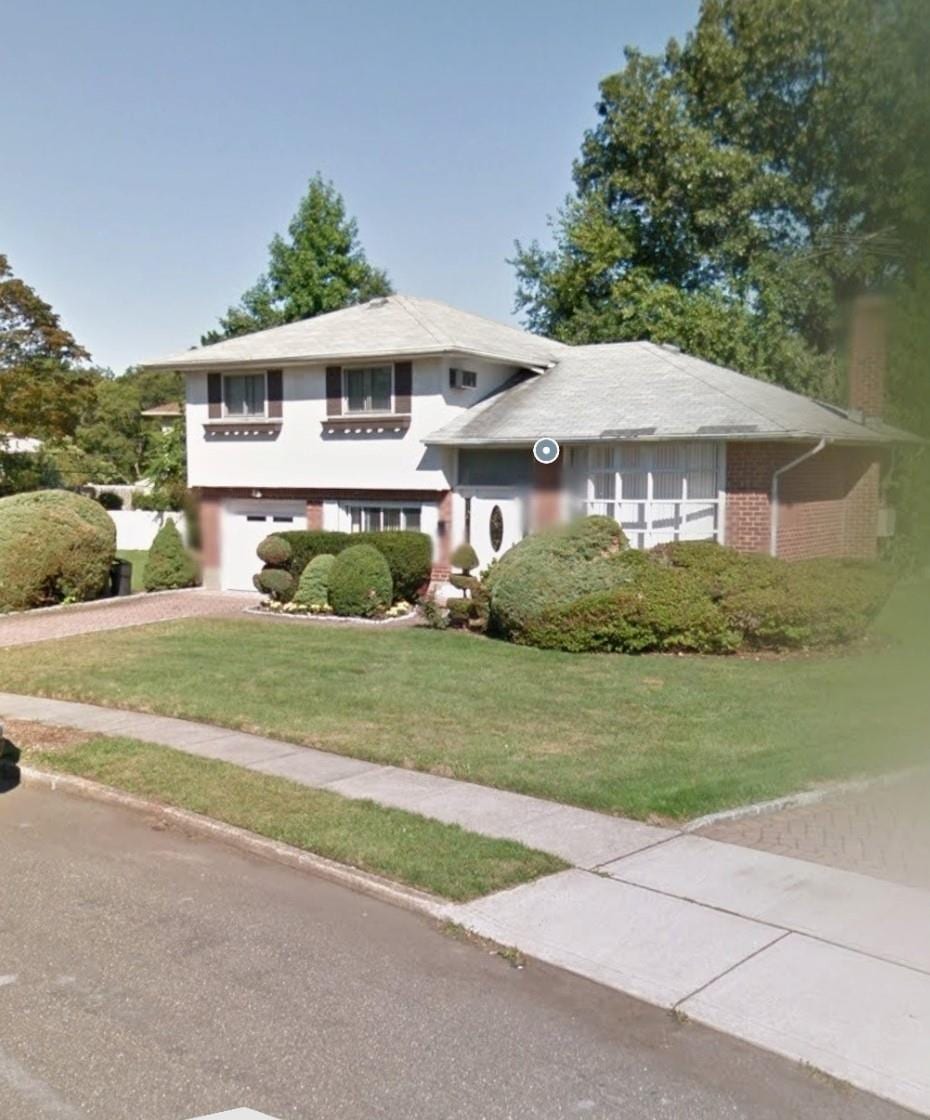 725 Carlisle Rd, Jericho, NY 11753 - tri-level home with driveway, a front lawn, an attached garage, and stucco siding