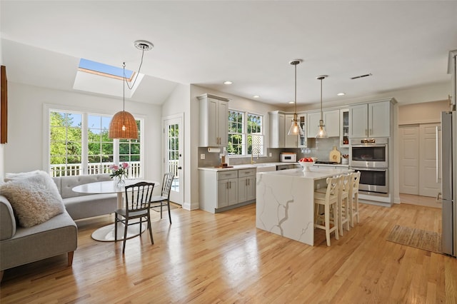 10 Inverness Ct, White Plains, NY 10605 - kitchen featuring appliances with stainless steel finishes, gray cabinetry, a skylight, light wood-style floors, and a breakfast bar area