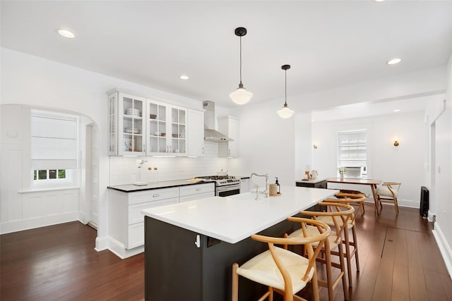 1223 Albany Post Rd, Croton-On-Hudson, NY 10520 - kitchen with wall chimney range hood, stainless steel gas range, dark wood-style flooring, glass insert cabinets, and a kitchen breakfast bar