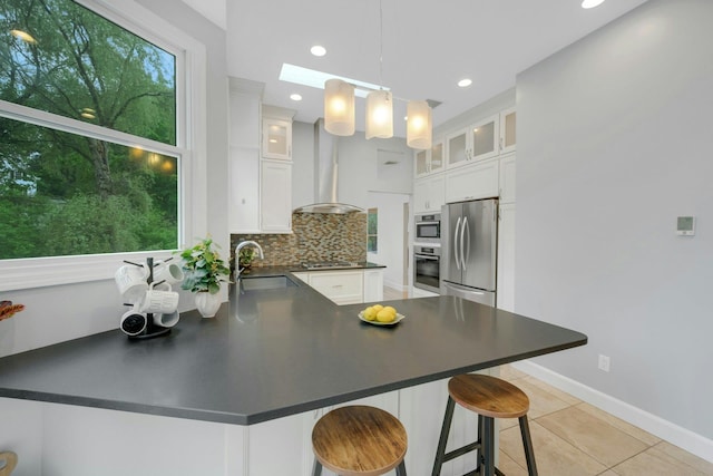 31 Pierce Dr, Pleasantville, NY 10570 - kitchen featuring appliances with stainless steel finishes, wall chimney range hood, a peninsula, white cabinets, and decorative backsplash
