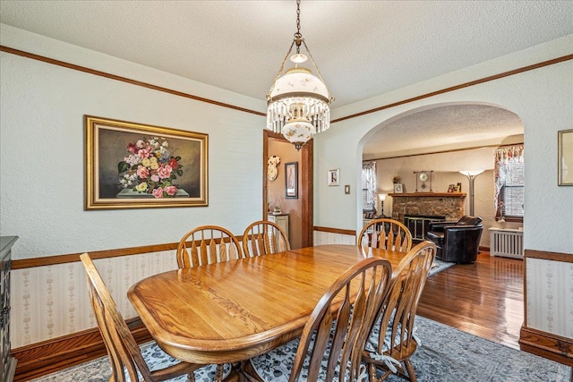 163-50 25th Dr, Flushing, NY 11358 - dining space featuring arched walkways, radiator heating unit, a textured ceiling, wood finished floors, and a fireplace