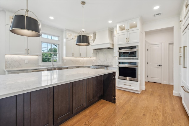 96A Calvin Ave, Syosset, NY 11791 - kitchen featuring custom range hood, stainless steel appliances, white cabinetry, light wood finished floors, and glass insert cabinets