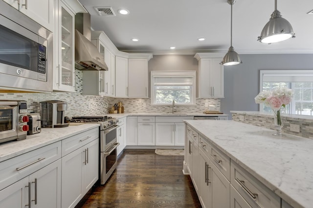28 Weir Ln, Locust Valley, NY 11560 - kitchen with appliances with stainless steel finishes, wall chimney range hood, backsplash, white cabinets, and ornamental molding