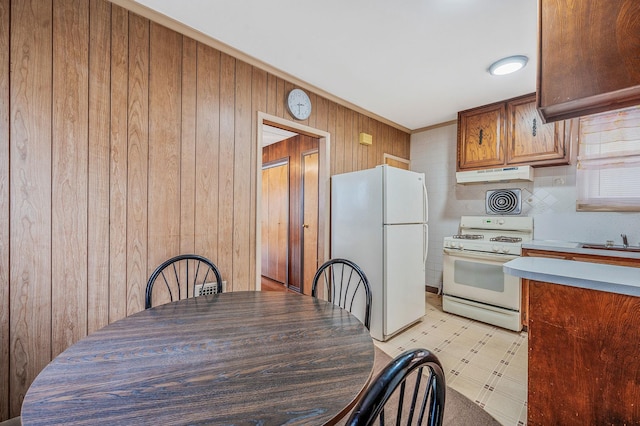 66-13 73rd Pl, Middle Village, NY 11379 - kitchen with white appliances, under cabinet range hood, wood walls, light floors, and crown molding