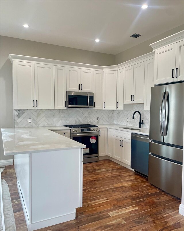 62 Clark St, Long Beach, NY 11561 - kitchen with appliances with stainless steel finishes, a peninsula, white cabinetry, dark wood-type flooring, and decorative backsplash