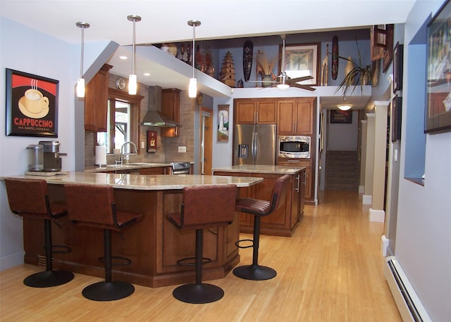 1778 Spur Dr S, Islip, NY 11751 - kitchen featuring appliances with stainless steel finishes, wall chimney exhaust hood, a baseboard radiator, a peninsula, and light wood finished floors