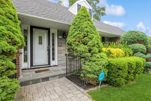 76 Roebling Pl E, Northport, NY 11731 - entrance to property with roof with shingles, stone siding, and covered porch