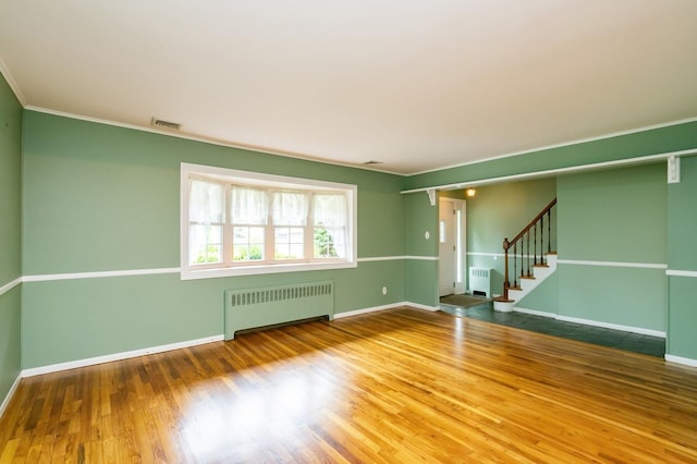 76 Roebling Pl E, Northport, NY 11731 - empty room with radiator heating unit, stairs, wood finished floors, and ornamental molding