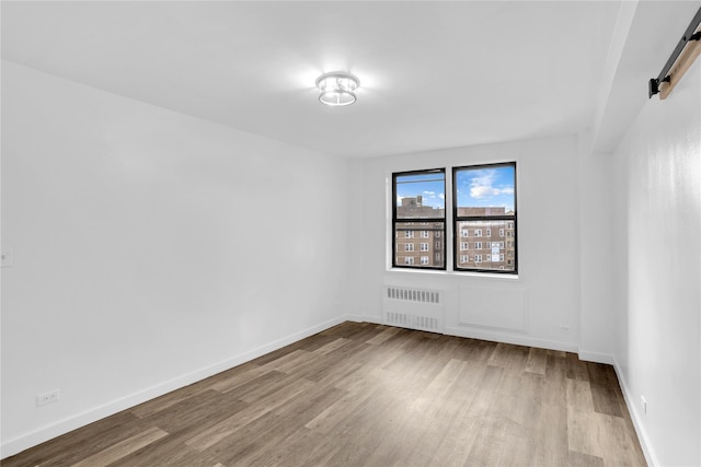 3184 Grand Unit 6D, Bronx, NY 10458 - spare room with radiator, a barn door, and wood finished floors