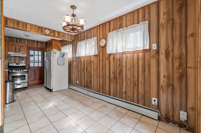 2354 7th St, East Meadow, NY 11554 - kitchen with stainless steel gas stove, freestanding refrigerator, baseboard heating, under cabinet range hood, and a chandelier