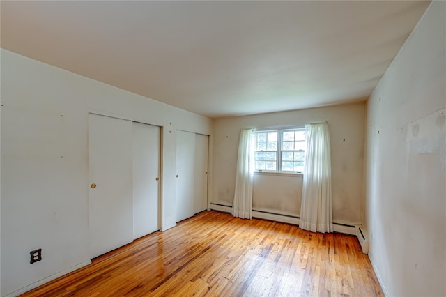 26 Village Ln, Hauppauge, NY 11788 - unfurnished bedroom featuring two closets, light wood-style flooring, and a baseboard heating unit