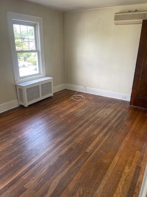 60 Hartsdale Rd, Elmsford, NY 10523 - empty room featuring radiator, a wall unit AC, and dark wood-style floors