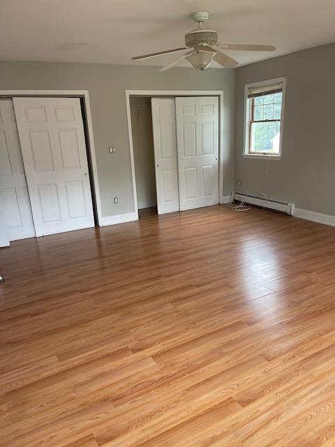 60 Hartsdale Rd, Elmsford, NY 10523 - unfurnished bedroom featuring a baseboard radiator, light wood finished floors, ceiling fan, and two closets