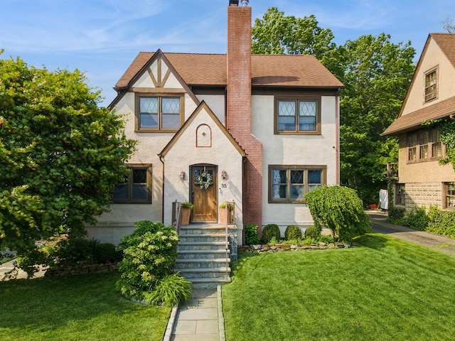 35 Irenhyl Ave, Port Chester, NY 10573 - tudor home featuring stucco siding, a chimney, a front yard, and roof with shingles