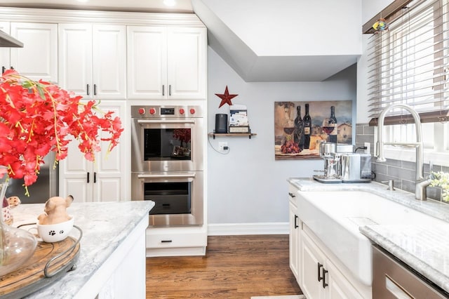 35 Irenhyl Ave, Port Chester, NY 10573 - kitchen with stainless steel double oven, light stone counters, white cabinetry, dark wood-style flooring, and backsplash