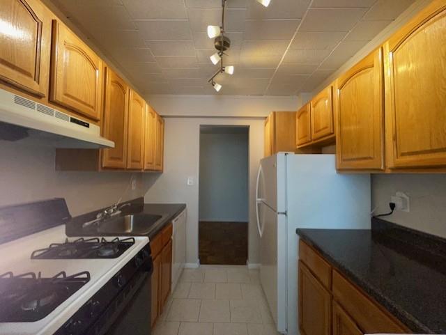 125 Main St Unit 2H, Port Washington, NY 11050 - kitchen with white appliances, under cabinet range hood, track lighting, light tile patterned floors, and dark countertops
