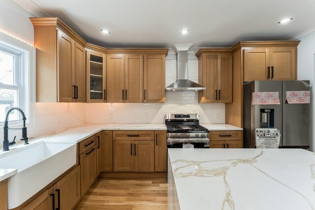 237 Linden Ave, Westbury, NY 11590 - kitchen with stainless steel appliances, wall chimney range hood, light wood-type flooring, light stone countertops, and glass insert cabinets