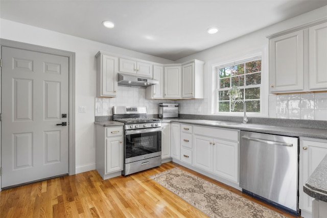 38 Southview Ct, Poughkeepsie, NY 12603 - kitchen featuring appliances with stainless steel finishes, under cabinet range hood, dark countertops, decorative backsplash, and light wood finished floors