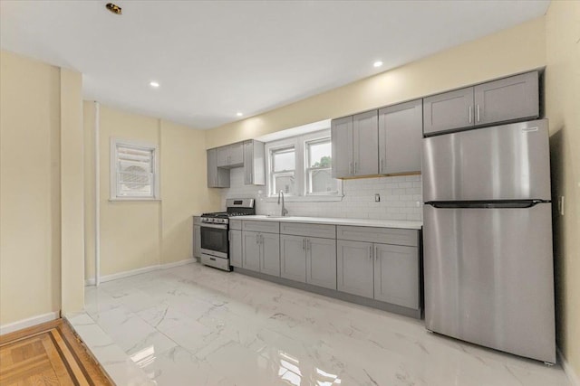 4216 Wickham Ave, Bronx, NY 10466 - kitchen with stainless steel appliances, gray cabinets, decorative backsplash, light countertops, and light marble finish floors