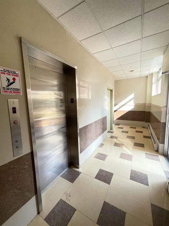 40-48 97th St Unit 3D, Corona, NY 11368 - hall featuring a paneled ceiling, elevator, baseboard heating, and light flooring
