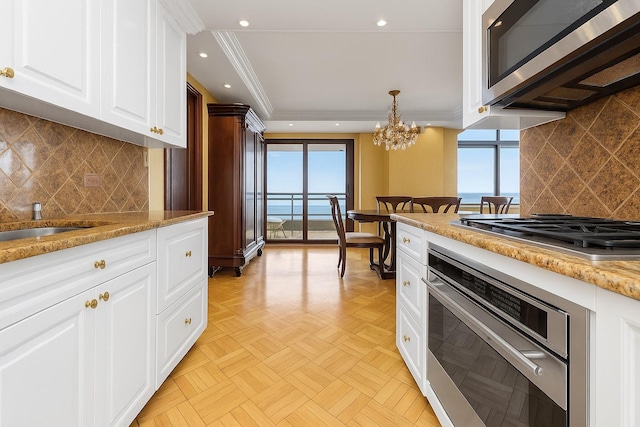 11201 Queens Blvd Unit 10B, Forest Hills, NY 11375 - kitchen featuring appliances with stainless steel finishes, a chandelier, white cabinetry, ornamental molding, and backsplash