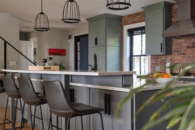 20 Paye Ave, Beacon, NY 12508 - kitchen featuring wall chimney range hood, decorative light fixtures, a breakfast bar area, brick wall, and a center island with sink