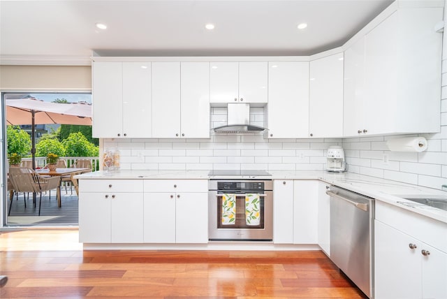 79 Fern St, New Rochelle, NY 10801 - kitchen featuring appliances with stainless steel finishes, exhaust hood, light wood-style flooring, white cabinetry, and backsplash