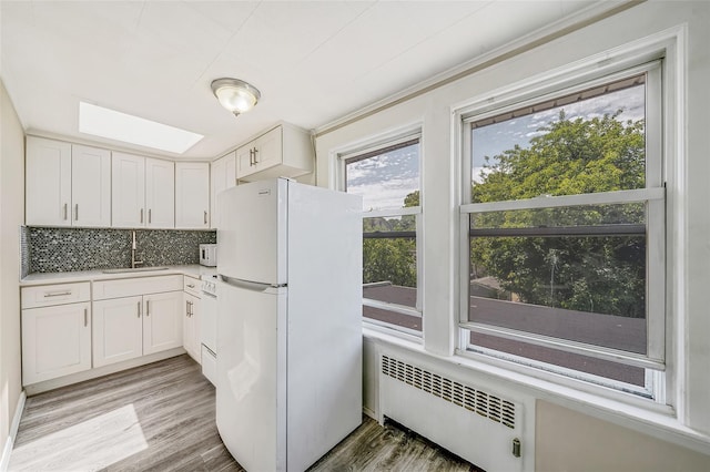 10 Leach St, Lynbrook, NY 11563 - kitchen featuring freestanding refrigerator, radiator, a skylight, backsplash, and white cabinetry