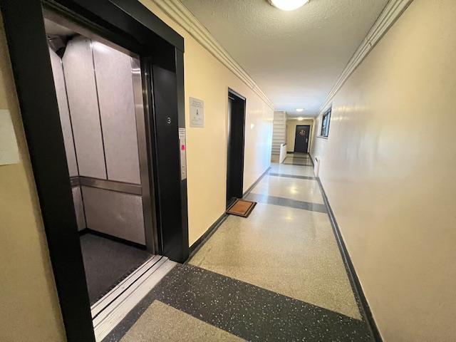 75-15 210th St Unit 2E, Bayside, NY 11364 - corridor featuring crown molding, speckled floor, elevator, and a textured ceiling