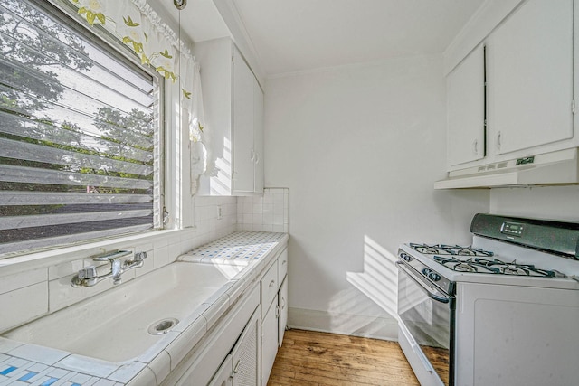 18803 Ilion Ave, Saint Albans, NY 11412 - kitchen featuring white range with gas stovetop, under cabinet range hood, light wood finished floors, white cabinets, and backsplash