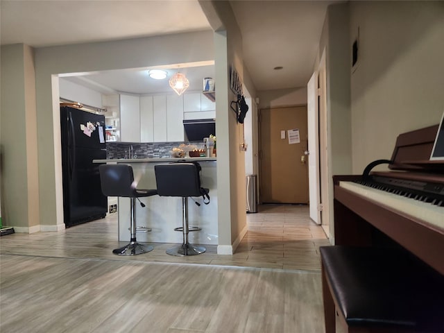 240-02 70th Ave Unit 1C, Douglaston, NY 11362 - kitchen with freestanding refrigerator, light wood-style flooring, tasteful backsplash, a kitchen bar, and white cabinetry