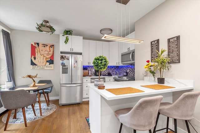 160-15 Powells Cove Blvd Unit B103, Beechhurst, NY 11357 - kitchen with appliances with stainless steel finishes, a kitchen breakfast bar, a peninsula, light wood-style flooring, and white cabinetry