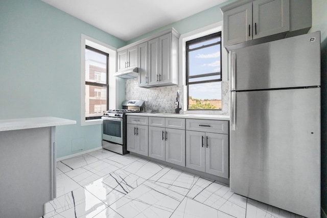 6050 71st Ave, Ridgewood, NY 11385 - kitchen featuring appliances with stainless steel finishes, gray cabinetry, under cabinet range hood, light countertops, and backsplash