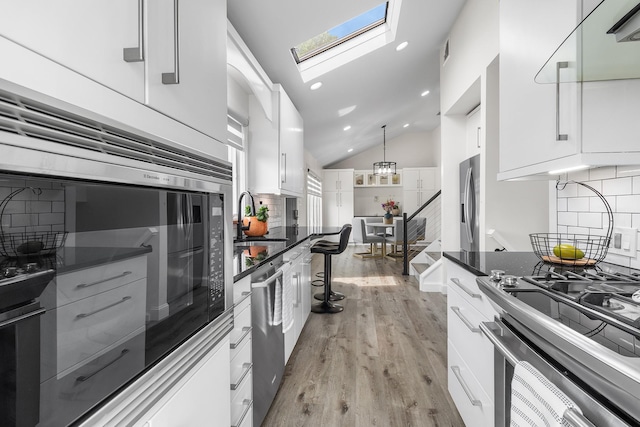 270 Farmers Ave, Lindenhurst, NY 11757 - kitchen with a skylight, vaulted ceiling, appliances with stainless steel finishes, white cabinets, and light wood-style floors