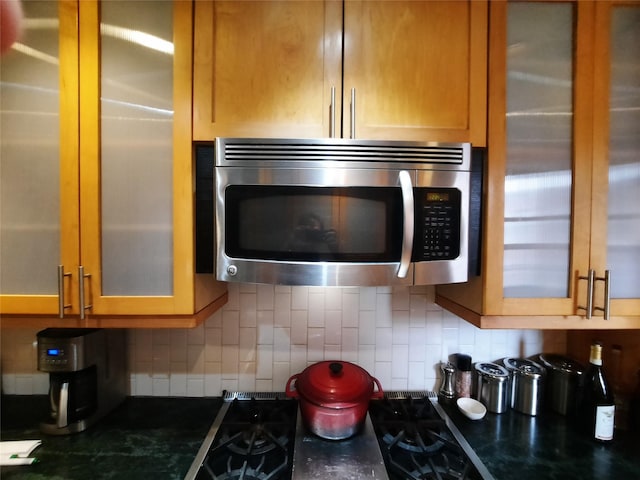 33-47 91st St Unit 5A, Jackson Heights, NY 11372 - kitchen featuring stainless steel microwave, glass insert cabinets, decorative backsplash, dark stone counters, and brown cabinetry