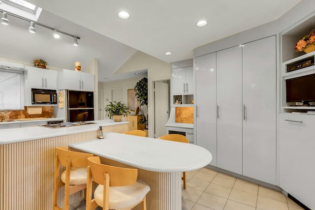 102 Bayview Ave, East Islip, NY 11730 - kitchen with black appliances, a breakfast bar area, lofted ceiling, light countertops, and light tile patterned floors
