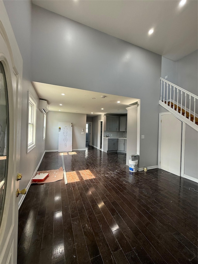 4006 Rockaway Beach Blvd, Edgemere, NY 11691 - unfurnished living room featuring a towering ceiling, a wall mounted AC, hardwood / wood-style floors, and stairs