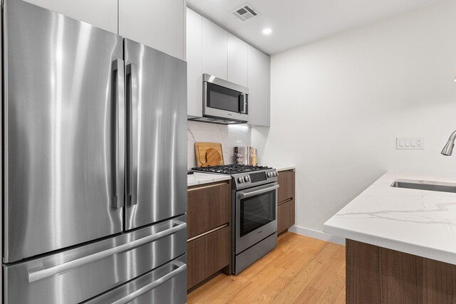 334 22nd St Unit 2B, Brooklyn, NY 11215 - kitchen featuring appliances with stainless steel finishes, light wood-type flooring, decorative backsplash, modern cabinets, and white cabinetry