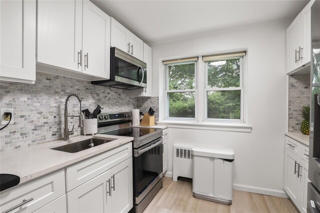 140 N Broadway Unit It9, Irvington, NY 10533 - kitchen featuring stainless steel appliances, light countertops, radiator, light wood finished floors, and white cabinetry