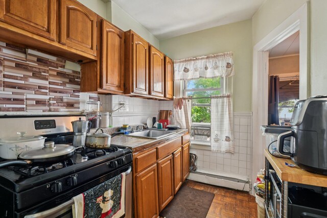 9406 76th St, Ozone Park, NY 11416 - kitchen featuring gas range, brown cabinets, light countertops, a wainscoted wall, and tile walls