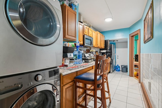 9406 76th St, Ozone Park, NY 11416 - laundry room featuring stacked washer and clothes dryer, light tile patterned floors, a wainscoted wall, and tile walls