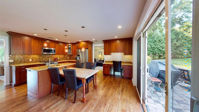 25 Mckinley St, Pearl River, NY 10965 - kitchen featuring appliances with stainless steel finishes, a kitchen island with sink, backsplash, light wood-style flooring, and light stone counters