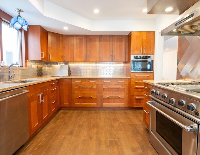 16107 90th St, Howard Beach, NY 11414 - kitchen featuring appliances with stainless steel finishes, wood finished floors, brown cabinetry, light stone countertops, and recessed lighting