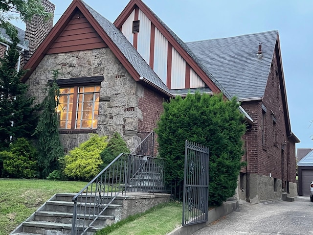 32-15 149th St, Flushing, NY 11354 - english style home featuring stairs, stone siding, a front lawn, a shingled roof, and brick siding