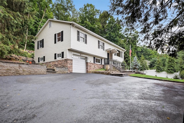 12 Valley Ln, Garrison, NY 10524 - view of front of house with stone siding, a garage, driveway, and view of scattered trees