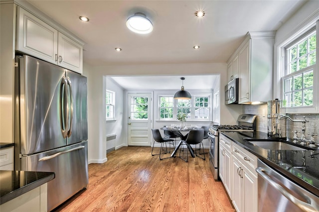 10 Cross St, Port Washington, NY 11050 - kitchen featuring appliances with stainless steel finishes, radiator, dark stone countertops, light wood finished floors, and decorative backsplash