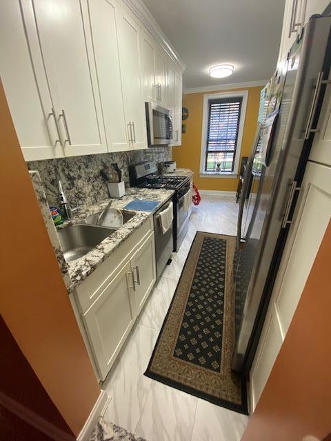 35-21 81st St Unit 1B, Jackson Heights, NY 11372 - kitchen with stainless steel appliances, ornamental molding, white cabinetry, backsplash, and light marble finish floors