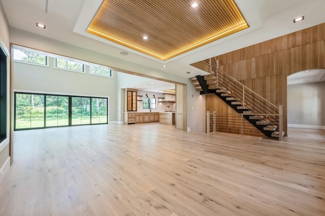 352 Cold Spring Rd, Syosset, NY 11791 - unfurnished living room featuring a tray ceiling, stairway, light wood-style floors, arched walkways, and a high ceiling