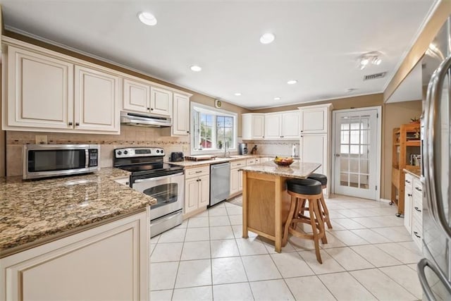 1 Cindy Ln, Highland Mills, NY 10930 - kitchen with appliances with stainless steel finishes, under cabinet range hood, tasteful backsplash, a breakfast bar, and light stone countertops