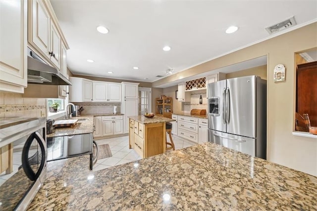 1 Cindy Ln, Highland Mills, NY 10930 - kitchen with stainless steel fridge, under cabinet range hood, tasteful backsplash, light stone counters, and a kitchen bar